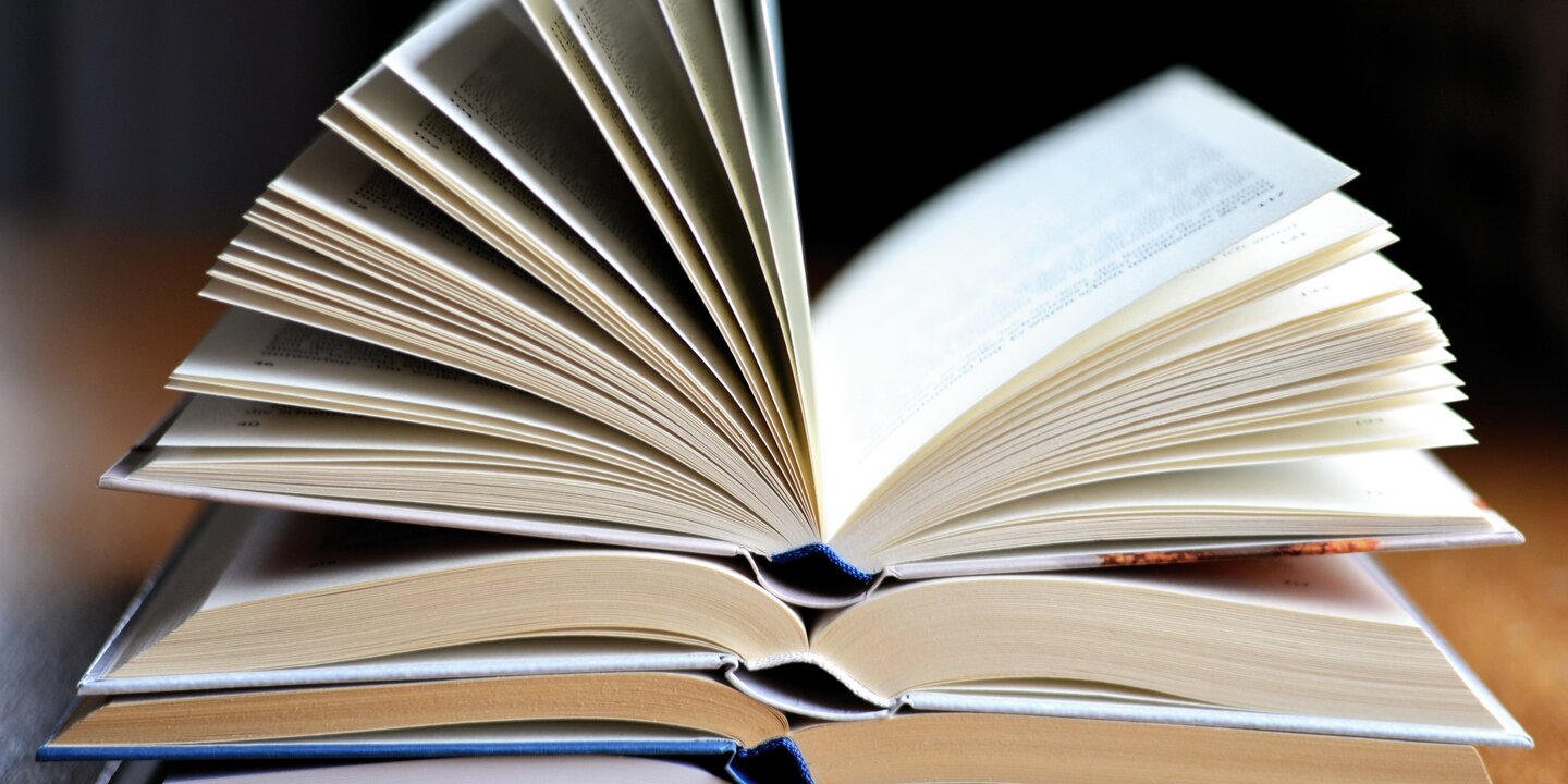 Auf einem Tisch liegt ein Stapel aufgeschlagener Bücher